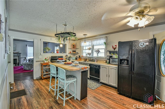 kitchen with wood counters, pendant lighting, a breakfast bar, white cabinets, and black appliances