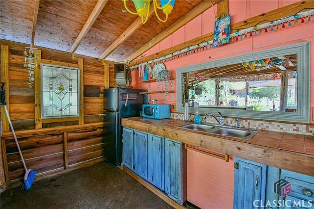 kitchen featuring wood walls, black fridge, sink, and vaulted ceiling