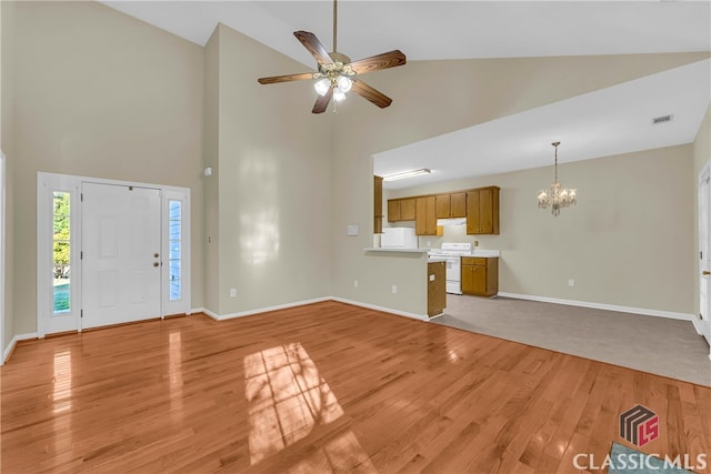 unfurnished living room featuring ceiling fan with notable chandelier, light wood-type flooring, and high vaulted ceiling