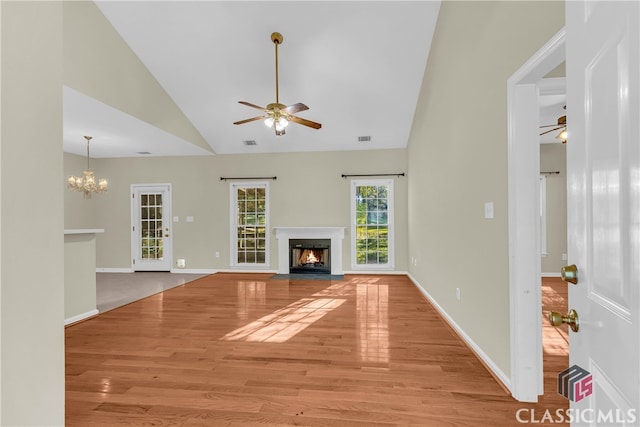 unfurnished living room with high vaulted ceiling, ceiling fan with notable chandelier, and light wood-type flooring