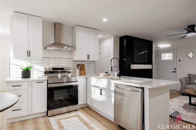 kitchen with kitchen peninsula, white cabinetry, wall chimney exhaust hood, and appliances with stainless steel finishes