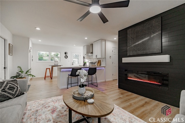 living room featuring light wood-type flooring, a large fireplace, and ceiling fan