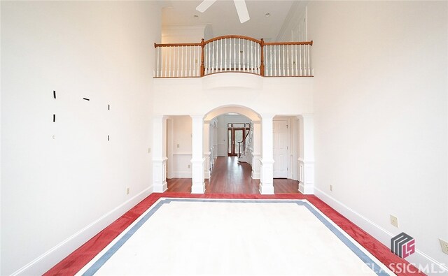 unfurnished room featuring a high ceiling, decorative columns, ceiling fan, and dark wood-type flooring