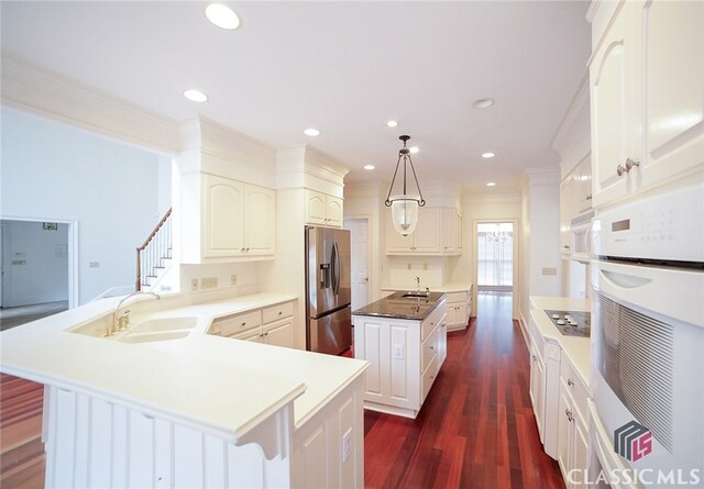 kitchen featuring white oven, sink, stainless steel fridge with ice dispenser, a kitchen island, and hanging light fixtures