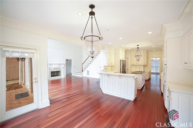 kitchen with ornamental molding, dark wood-type flooring, white cabinets, stainless steel fridge with ice dispenser, and hanging light fixtures