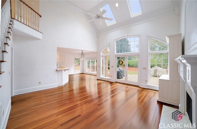 unfurnished living room with a skylight, ceiling fan, crown molding, hardwood / wood-style flooring, and high vaulted ceiling