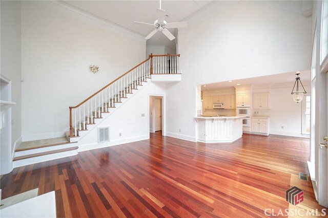 unfurnished living room with hardwood / wood-style floors, ceiling fan, a towering ceiling, and crown molding