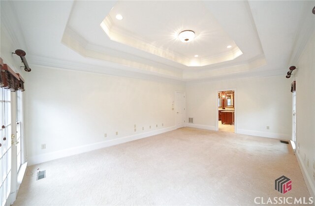 empty room with a tray ceiling, light colored carpet, and ornamental molding