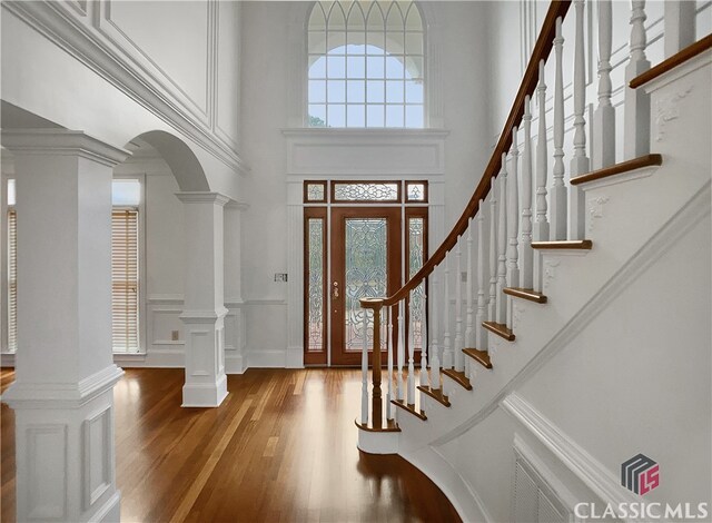 foyer entrance featuring wood-type flooring, a towering ceiling, ornate columns, and ornamental molding