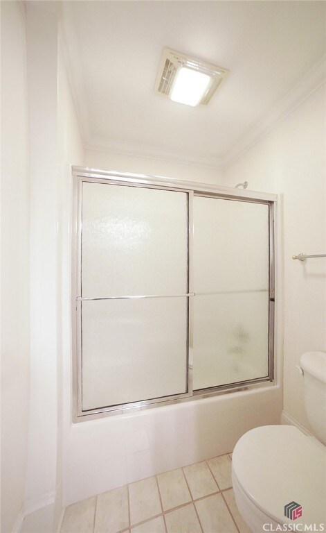 bathroom featuring tile patterned flooring, toilet, ornamental molding, and bath / shower combo with glass door