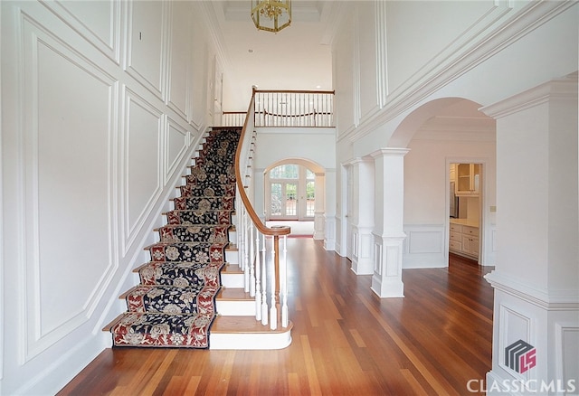 staircase featuring crown molding, french doors, a towering ceiling, and wood-type flooring