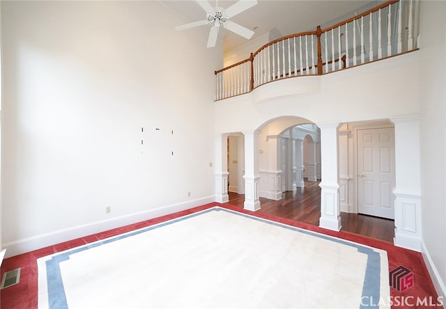 interior space with decorative columns, ceiling fan, a towering ceiling, and dark hardwood / wood-style floors