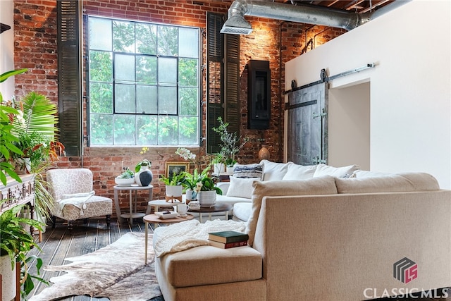 living room featuring a barn door, wood-type flooring, and brick wall