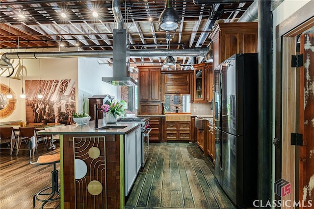 kitchen featuring a center island with sink, black refrigerator, high end range, sink, and dark hardwood / wood-style floors