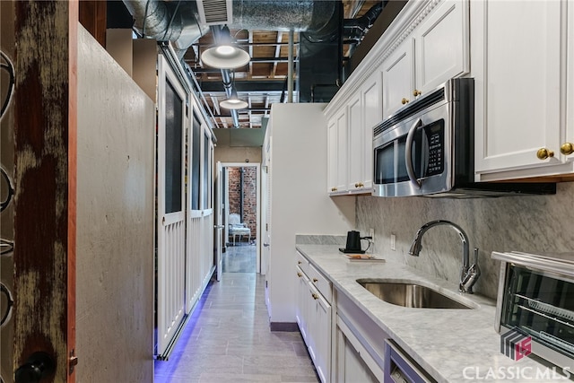 kitchen with sink, tasteful backsplash, white cabinets, and light stone counters