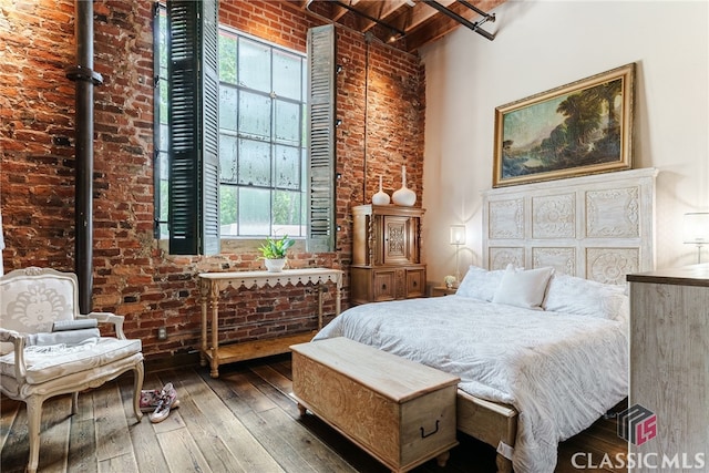 bedroom with hardwood / wood-style flooring, a towering ceiling, and brick wall