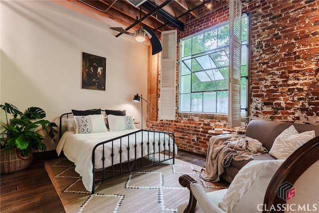 bedroom with beam ceiling, brick wall, and wood-type flooring