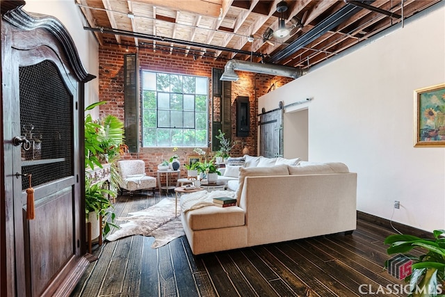 living room with brick wall, dark hardwood / wood-style flooring, and a barn door