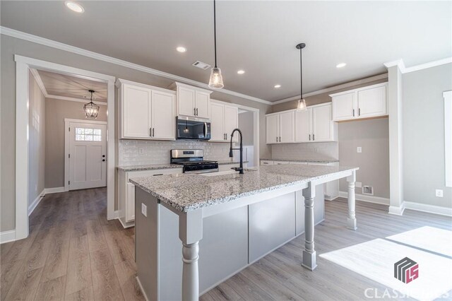 kitchen with light stone countertops, white cabinets, a kitchen island with sink, and appliances with stainless steel finishes