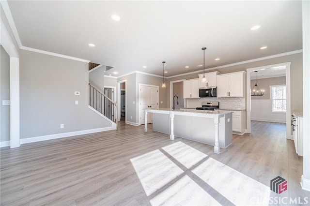 kitchen with white cabinets, a kitchen bar, stainless steel appliances, hanging light fixtures, and a center island with sink