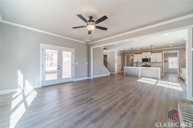 unfurnished living room featuring french doors, sink, ornamental molding, light wood-type flooring, and ceiling fan