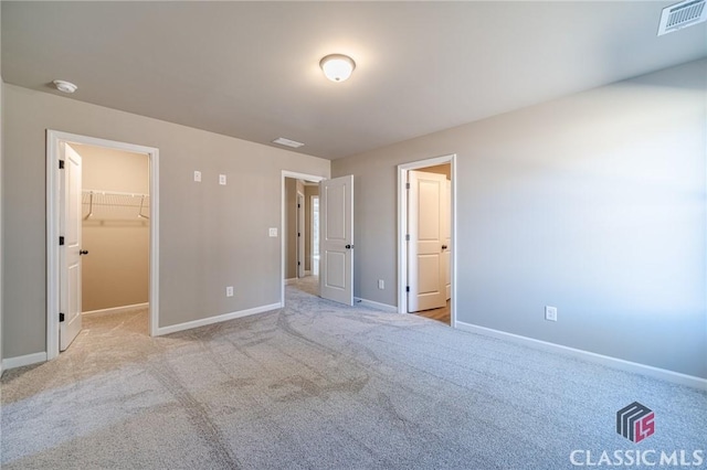 unfurnished bedroom featuring a walk in closet, a closet, and light colored carpet