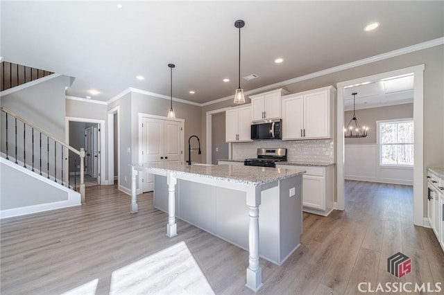 kitchen with stainless steel appliances, a kitchen bar, white cabinetry, and a kitchen island with sink