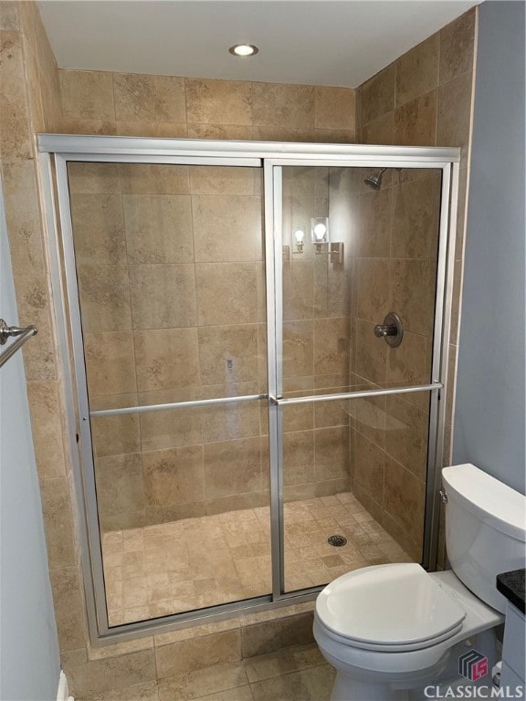 bathroom featuring toilet, tile patterned floors, and a shower with door