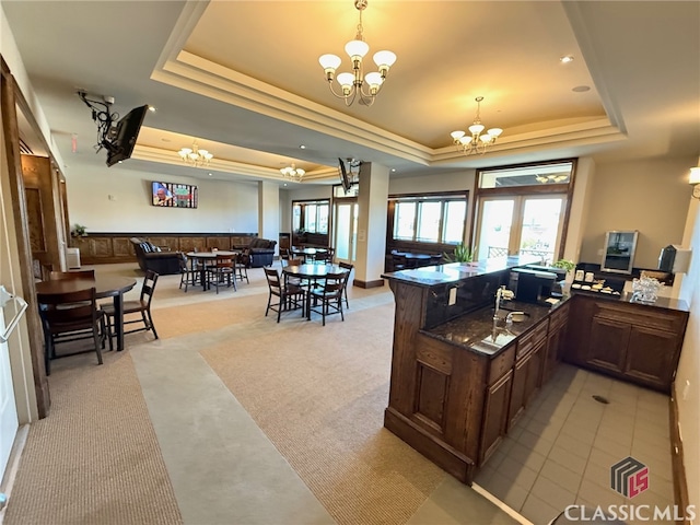 kitchen featuring a raised ceiling, kitchen peninsula, light carpet, and a notable chandelier