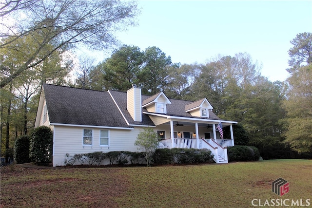 new england style home featuring covered porch, roof with shingles, a chimney, and a front yard