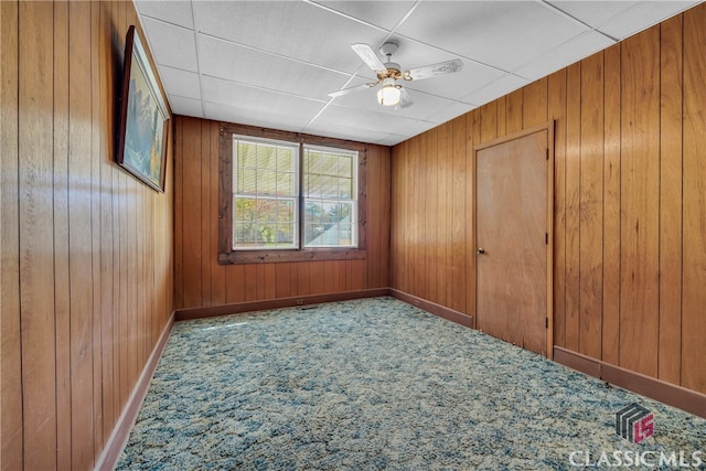 carpeted empty room with ceiling fan and wood walls