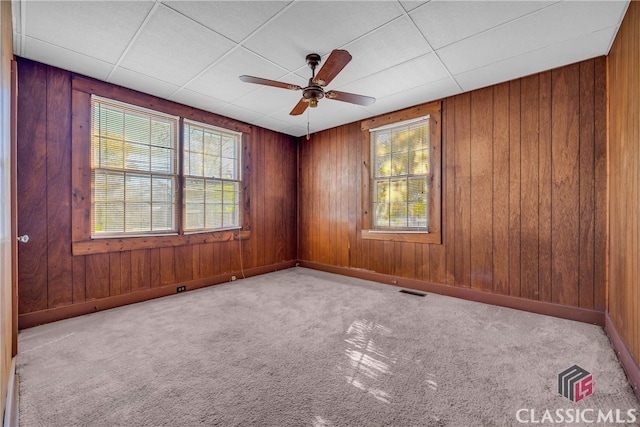 unfurnished room with wood walls, a drop ceiling, ceiling fan, and light colored carpet