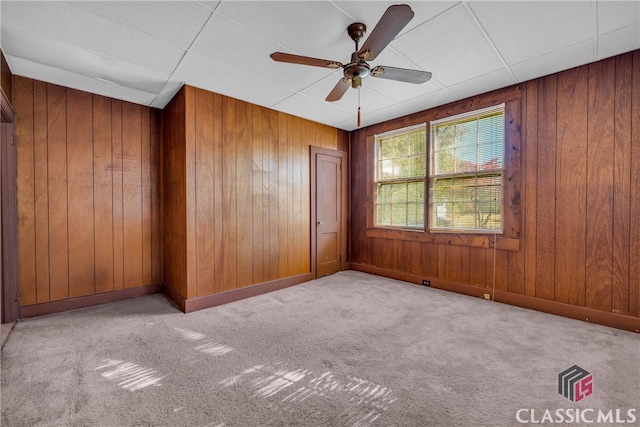 spare room featuring ceiling fan, wood walls, and light colored carpet