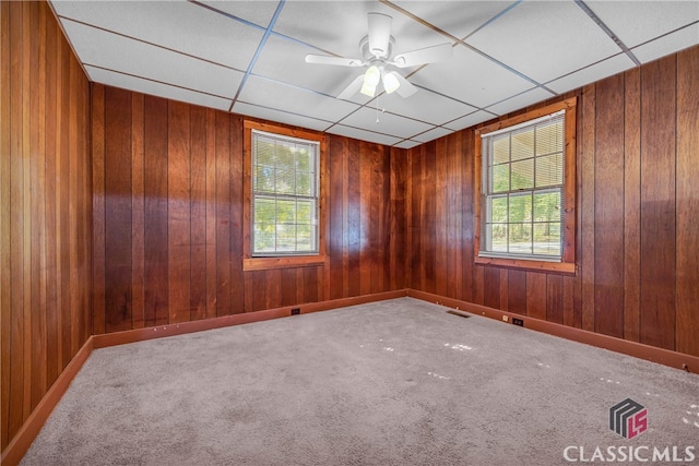 spare room featuring carpet, a drop ceiling, a wealth of natural light, and wood walls