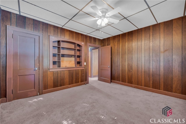 spare room with light colored carpet, built in features, ceiling fan, and wooden walls