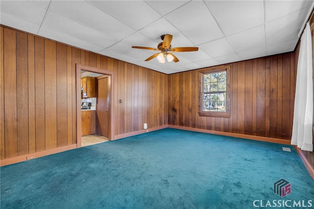 carpeted spare room with a paneled ceiling, ceiling fan, and wood walls