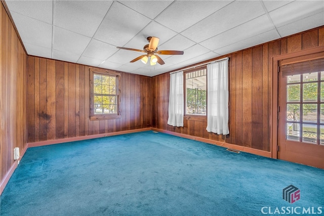 carpeted empty room with a wealth of natural light, wooden walls, and ceiling fan