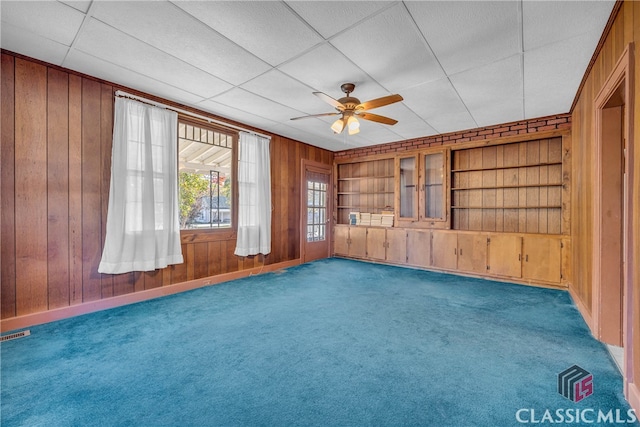 unfurnished living room featuring wood walls, ceiling fan, and dark carpet