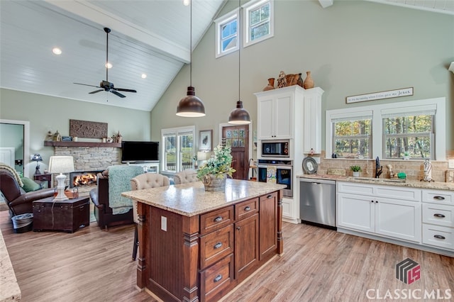 kitchen with pendant lighting, high vaulted ceiling, sink, white cabinetry, and stainless steel appliances