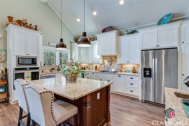 kitchen featuring appliances with stainless steel finishes, light wood-type flooring, light stone counters, decorative light fixtures, and white cabinets