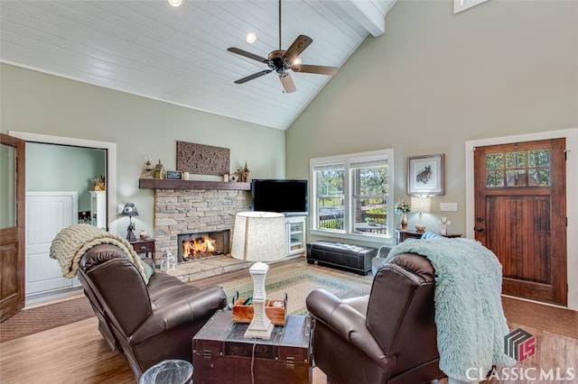 living room featuring high vaulted ceiling, a stone fireplace, ceiling fan, light wood-type flooring, and beam ceiling