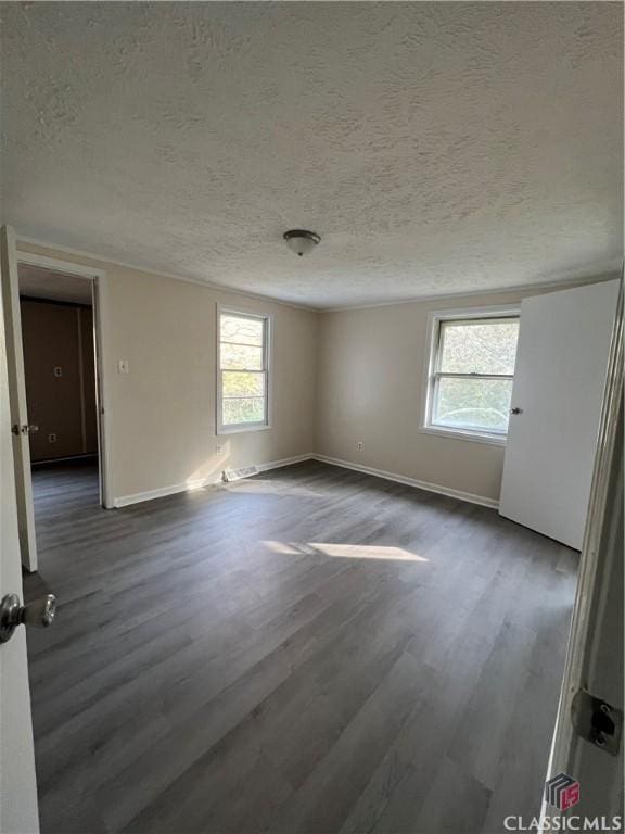 spare room with a textured ceiling, a wealth of natural light, and dark hardwood / wood-style floors