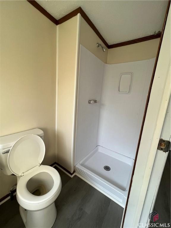 bathroom with crown molding, toilet, a shower, and a textured ceiling