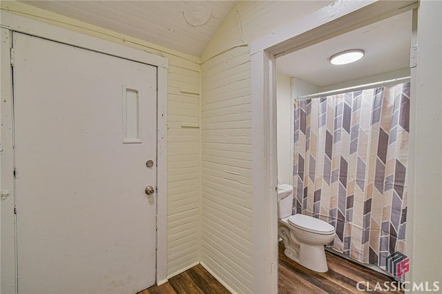 bathroom with vaulted ceiling, hardwood / wood-style flooring, tile walls, toilet, and wood walls