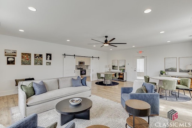 living room with a barn door, ceiling fan, and light hardwood / wood-style floors