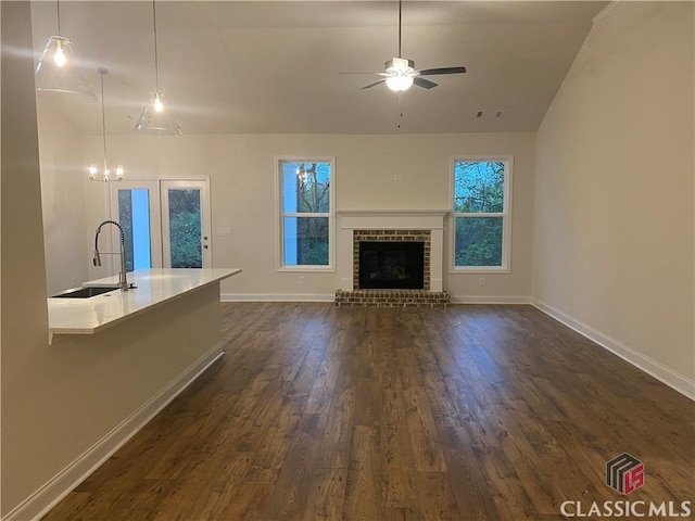 unfurnished living room featuring ceiling fan with notable chandelier, dark hardwood / wood-style flooring, sink, and a brick fireplace