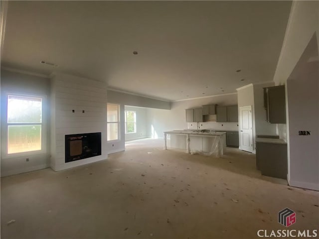 unfurnished living room with a large fireplace, crown molding, and sink