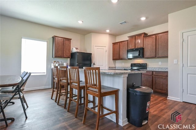 kitchen with light stone countertops, a kitchen breakfast bar, dark hardwood / wood-style flooring, black appliances, and a kitchen island