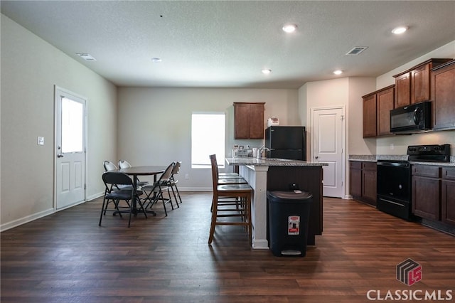 kitchen with an island with sink, a breakfast bar area, a healthy amount of sunlight, and black appliances