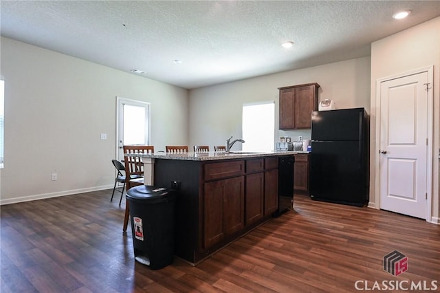 kitchen with dark hardwood / wood-style flooring, an island with sink, a textured ceiling, dark brown cabinets, and black appliances